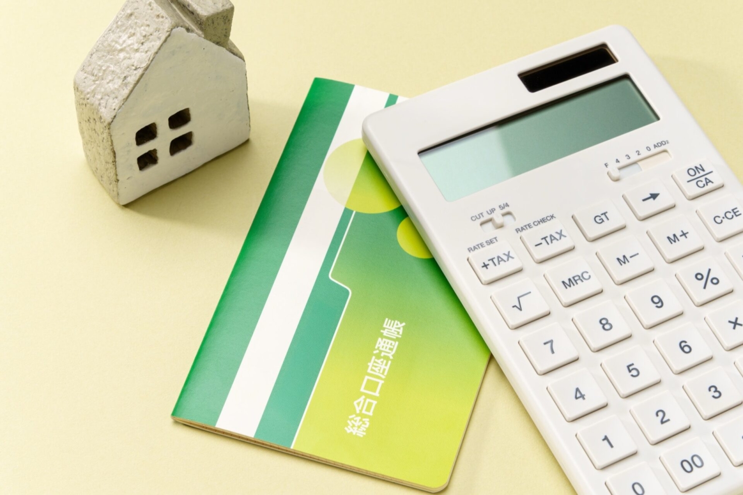 電卓と預金通帳とミニチュアの家